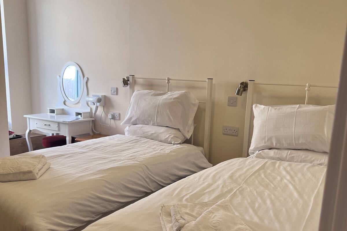 A hotel room with two beds, a bedside table with a mirror, and a hairdryer.