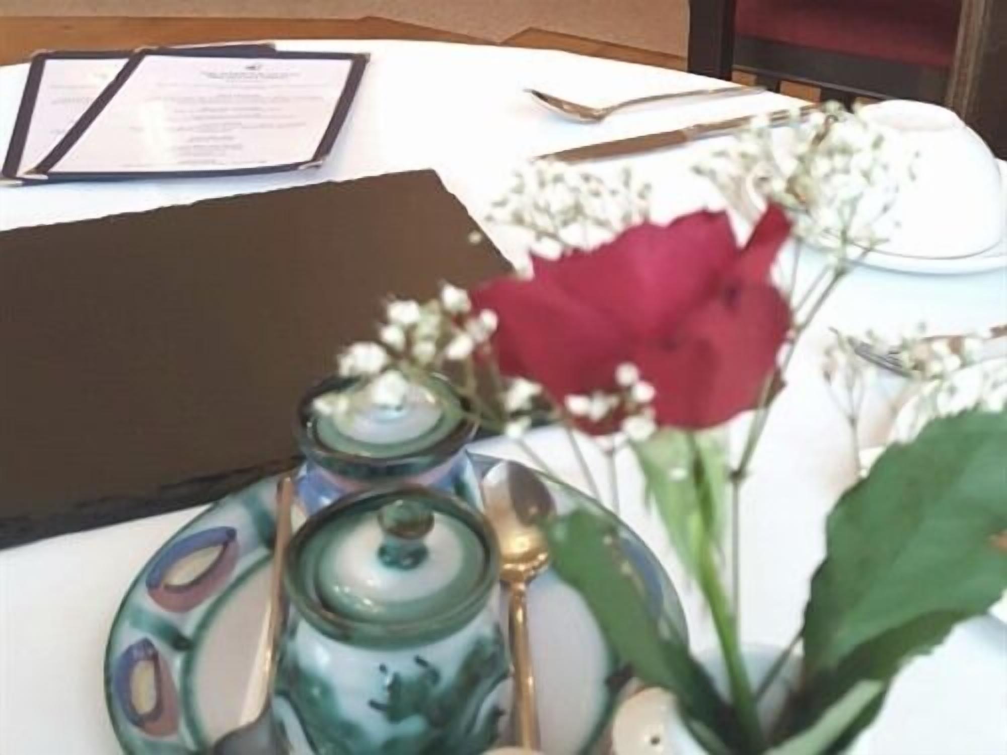 A table with a menu, a vase with a red flower, and a small green container.