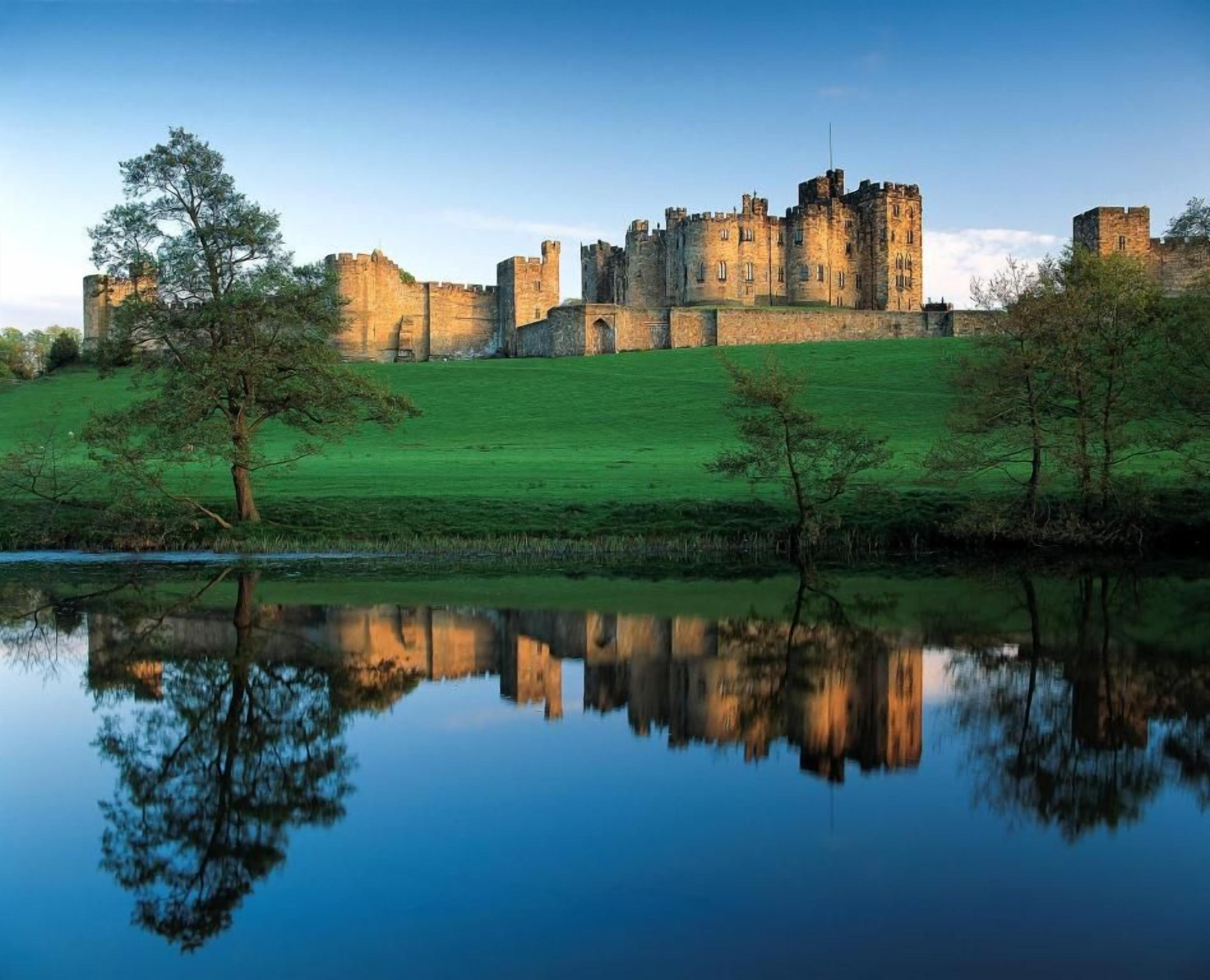 A castle with a moat, surrounded by green fields and trees.