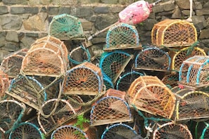 A collection of stacked lobster traps against a stone wall.