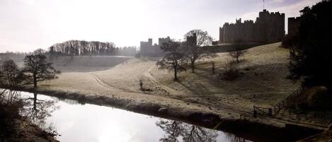 A castle on a hill overlooking a calm body of water with a path leading to it.