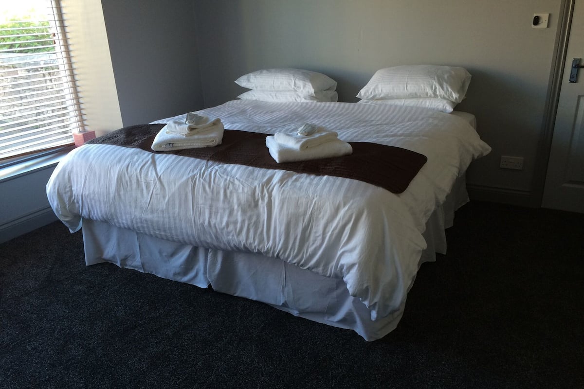 Quarto de hotel com uma cama grande, duas almofadas e uma toalha dobrada na cama.