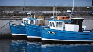 Two boats docked at a pier with a rocky shoreline in the background.