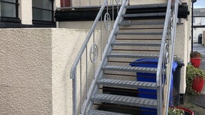 A metal staircase leading to a building entrance with a textured wall, a red door, and potted plants.
