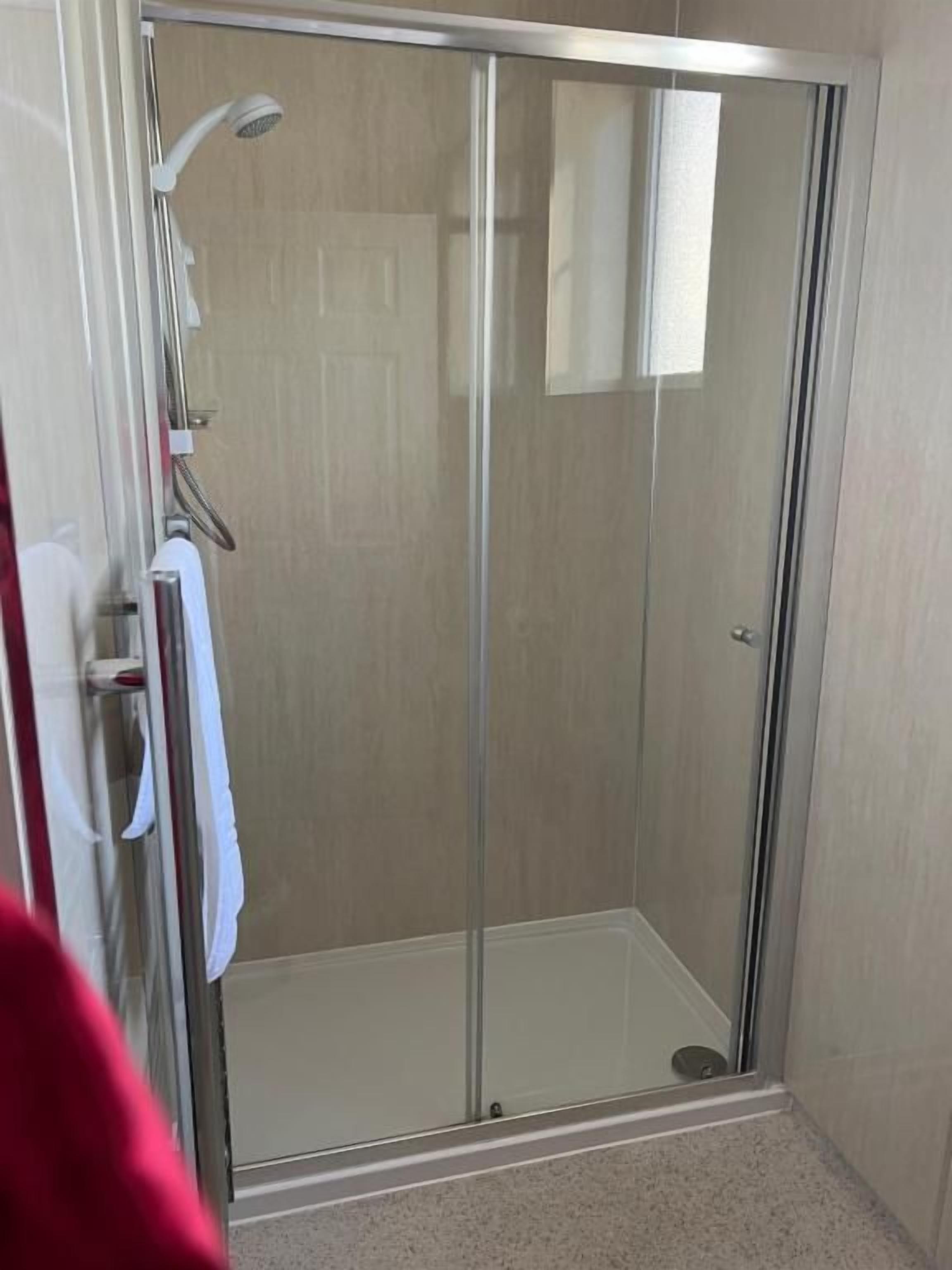 A glass-enclosed shower stall with a showerhead and a towel rack.