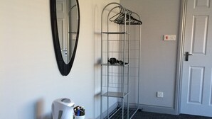 A room with a wooden table, a white kettle, and a metal shelf unit against a white wall.