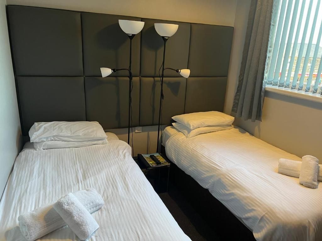 Habitación de hotel con dos camas, cabecera con iluminación integrada y ventana con persianas.