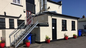 A building with a staircase leading to a door, potted plants, and a blue bin.