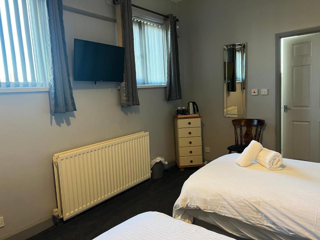 A hotel room with a bed, a dresser, a radiator, a television, and a window with curtains.
