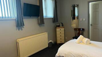 A hotel room with a bed, a dresser, a radiator, a television, and a window with curtains.