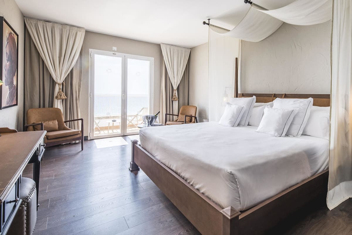 Ein Hotelzimmer mit einem großen Bett, einem Schreibtisch, einem Stuhl und einem Balkon mit Vorhängen.
