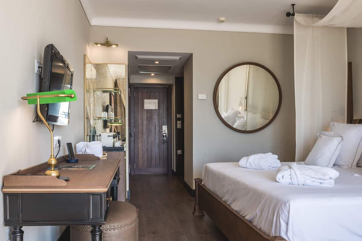 Ein Hotelzimmer mit Bett, Schreibtisch mit Lampe, Spiegel und einer Tür zu einem anderen Raum.