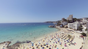 Una playa con numerosos sombrillas y gente, un cielo azul despejado y edificios a lo largo de la costa.