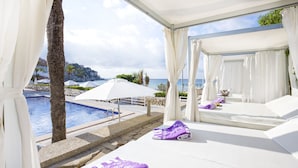 Un área de descanso junto a la piscina con toldos blancos, una piscina y vistas al mar.
