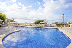 A swimming pool with lounge chairs and umbrellas, surrounded by a stone wall and a fence. - Be Live Adults Only La Cala Boutique Hotel (Palma de Mallorca)