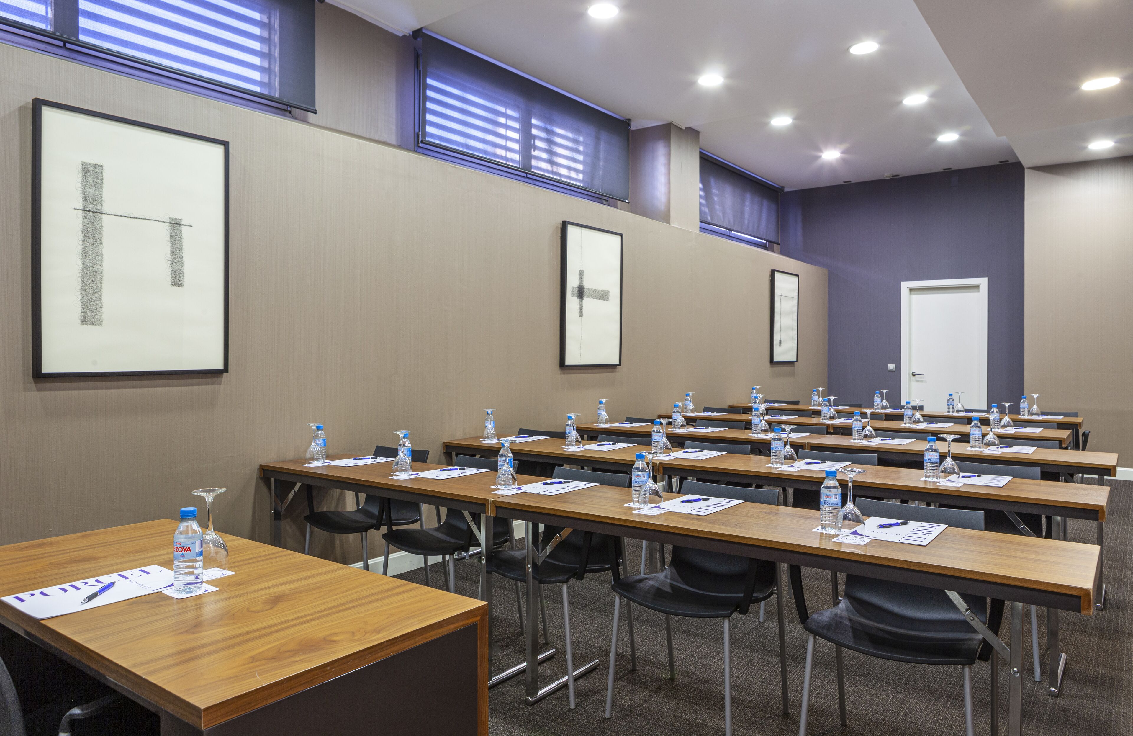 Un salón de conferencias con varias mesas, sillas, botellas de agua y material de presentación.