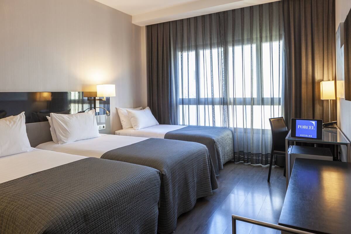 A hotel room with two beds, a desk, and a TV displaying "PORCEL".
