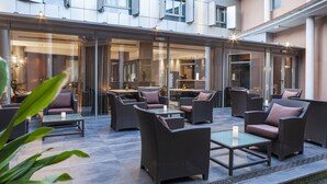 An outdoor seating area with wicker furniture and glass tables, overlooking a modern building with large windows and a well-lit interior. - Hotel Porcel Torneo (Seville)