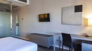 Habitación de hotel con cama, escritorio, silla, televisor y una obra de arte colgada en la pared.
