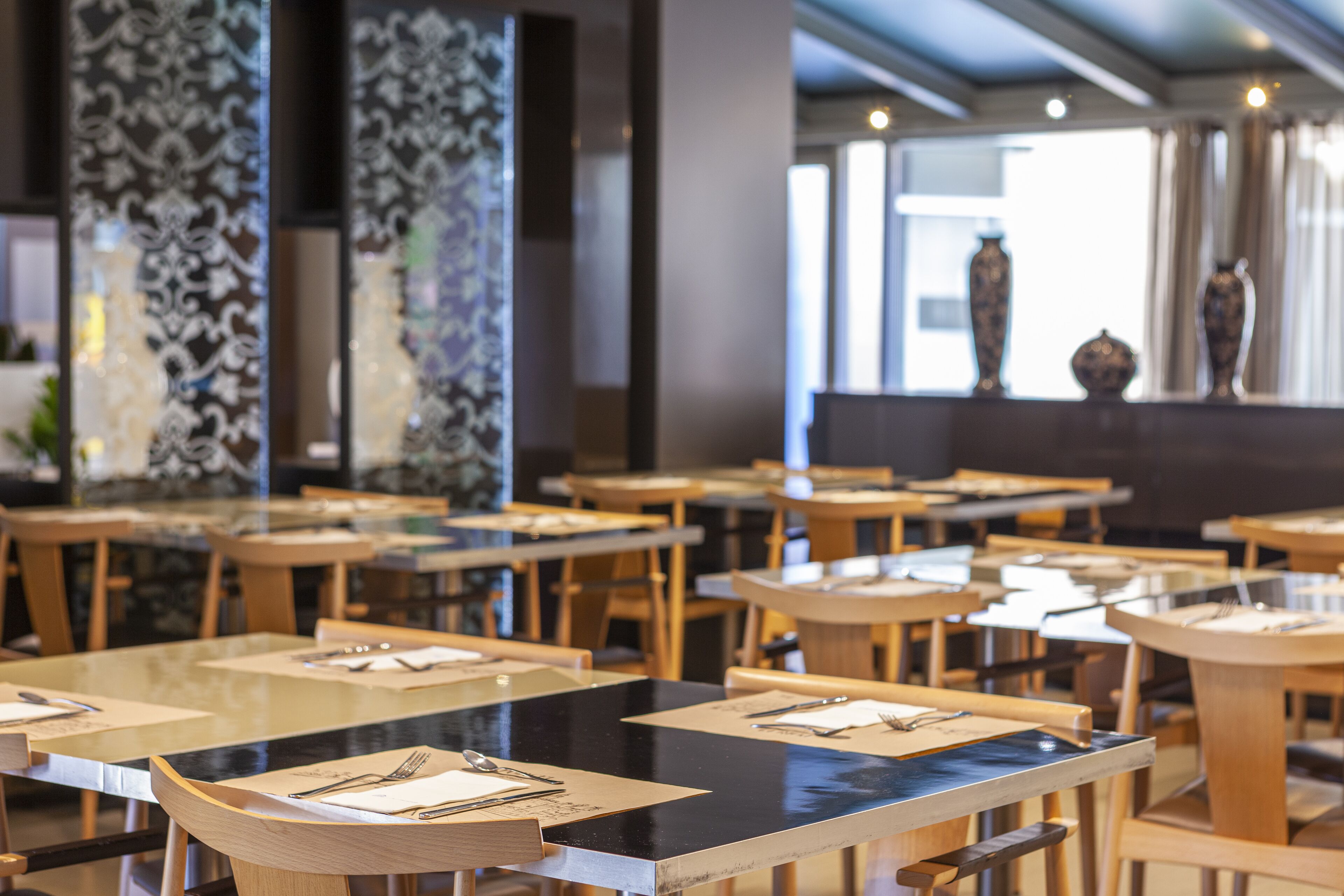 A restaurant with multiple tables and chairs, some with menus and cutlery.