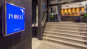 A hotel entrance with a blue sign reading "PORCEL", a staircase leading to the lobby, and a reception area with a wooden wall and decorative elements. - Hotel Porcel Torneo (Seville)