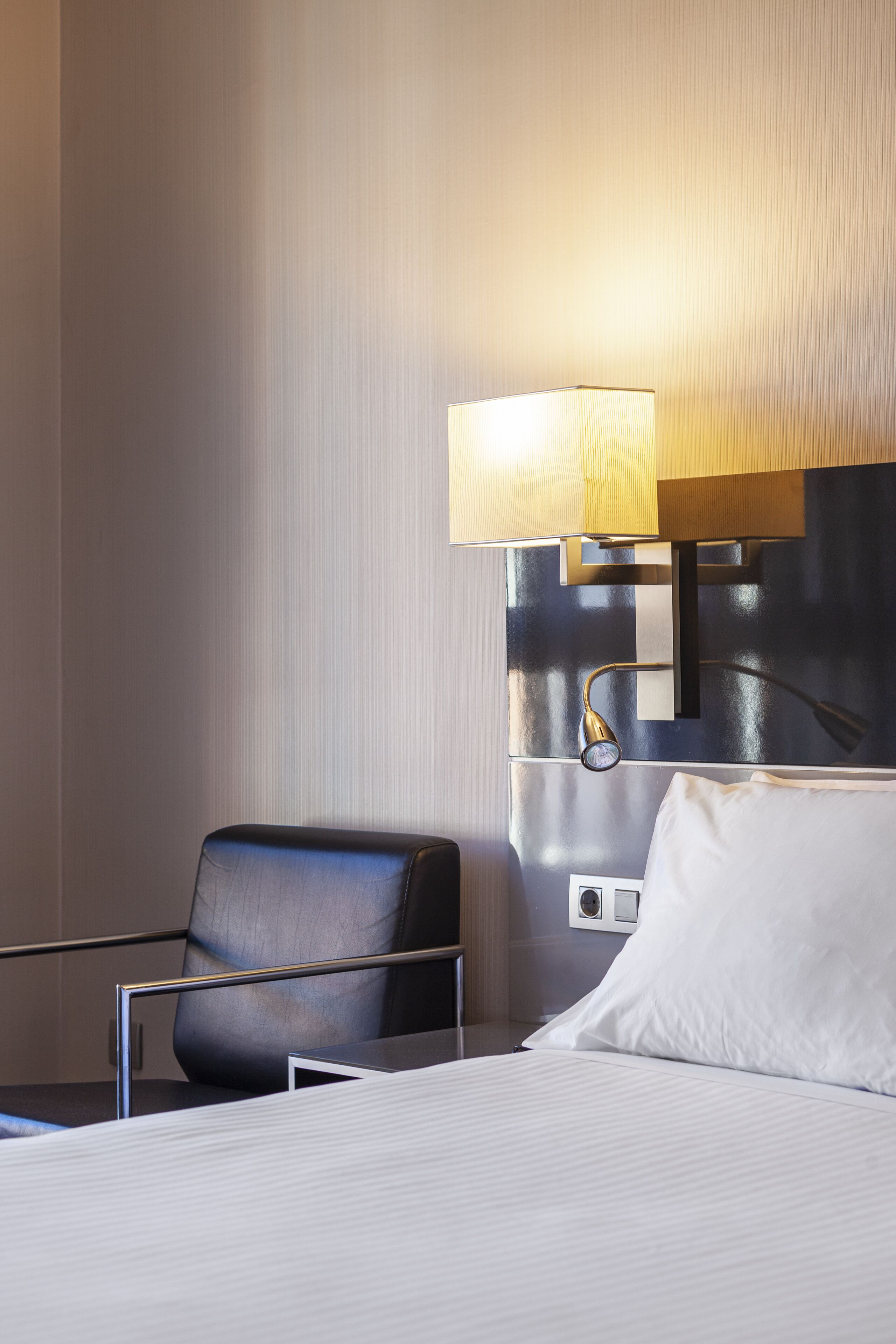 Una habitación de hotel con cama, mesita de noche, lámpara y silla.