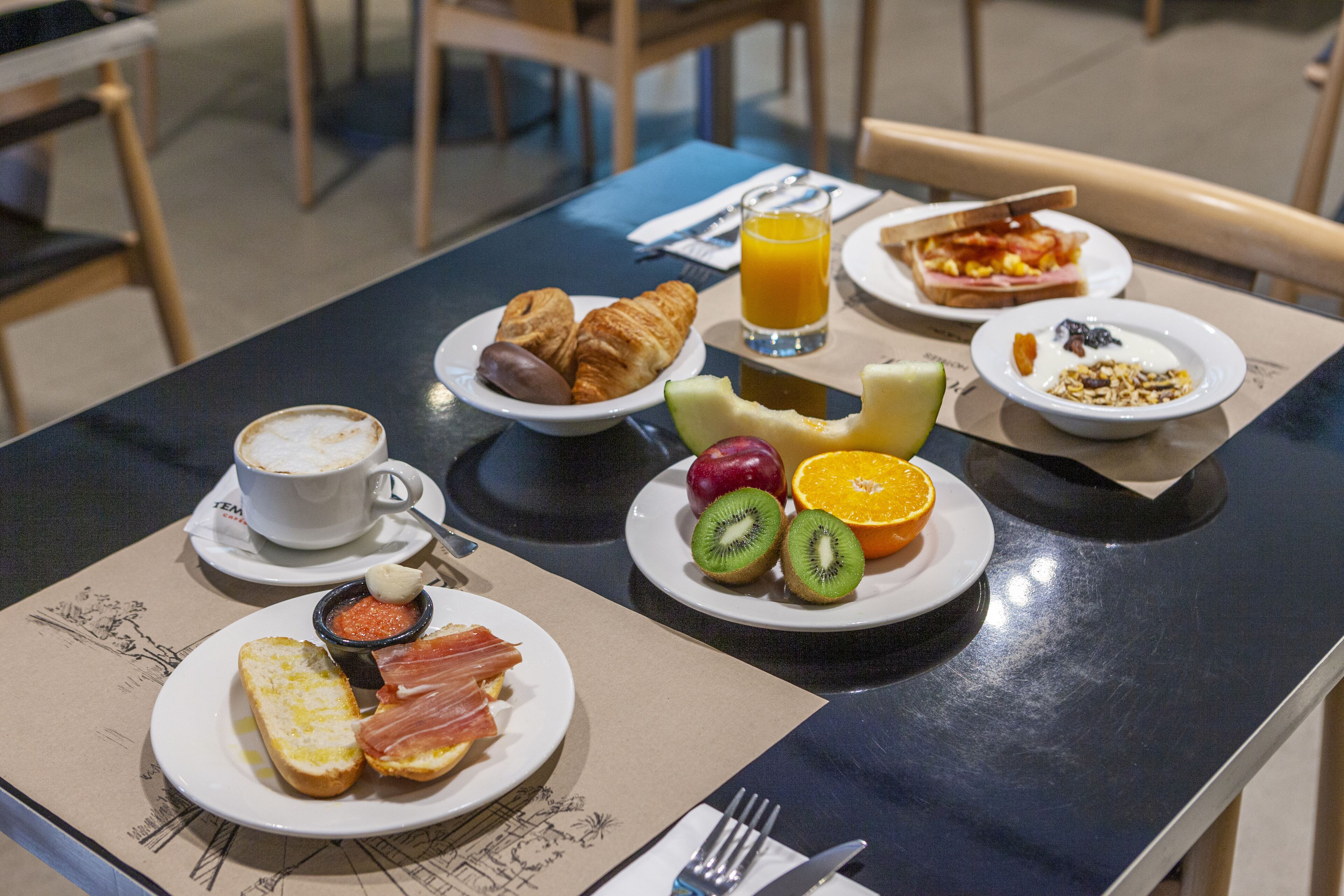 Un desayuno con cruasanes, fruta y una taza de café sobre una mesa.