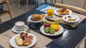 Un desayuno con cruasanes, fruta y una taza de café sobre una mesa.