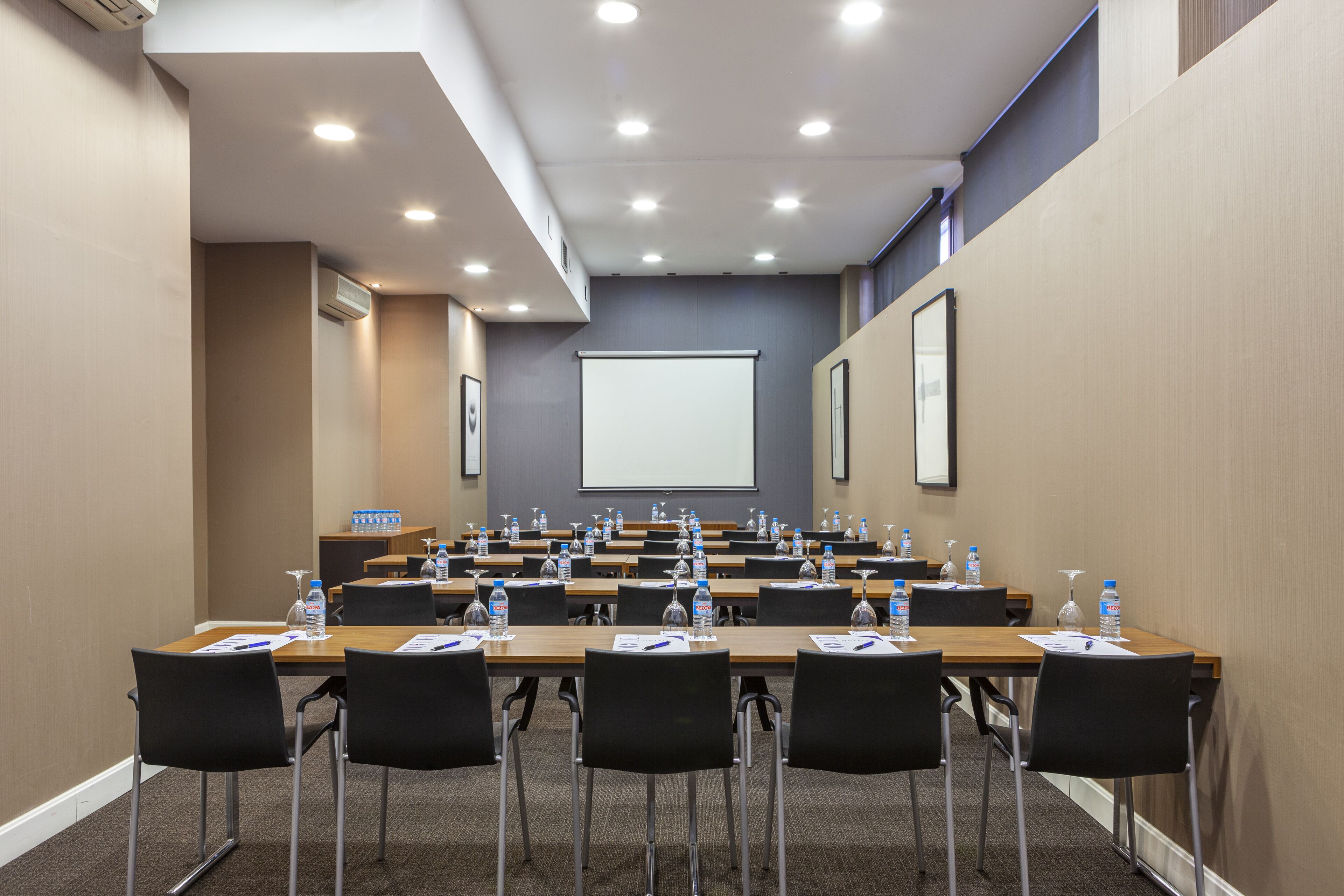 Una sala de conferencias con varias mesas, sillas y una pantalla para proyector.
