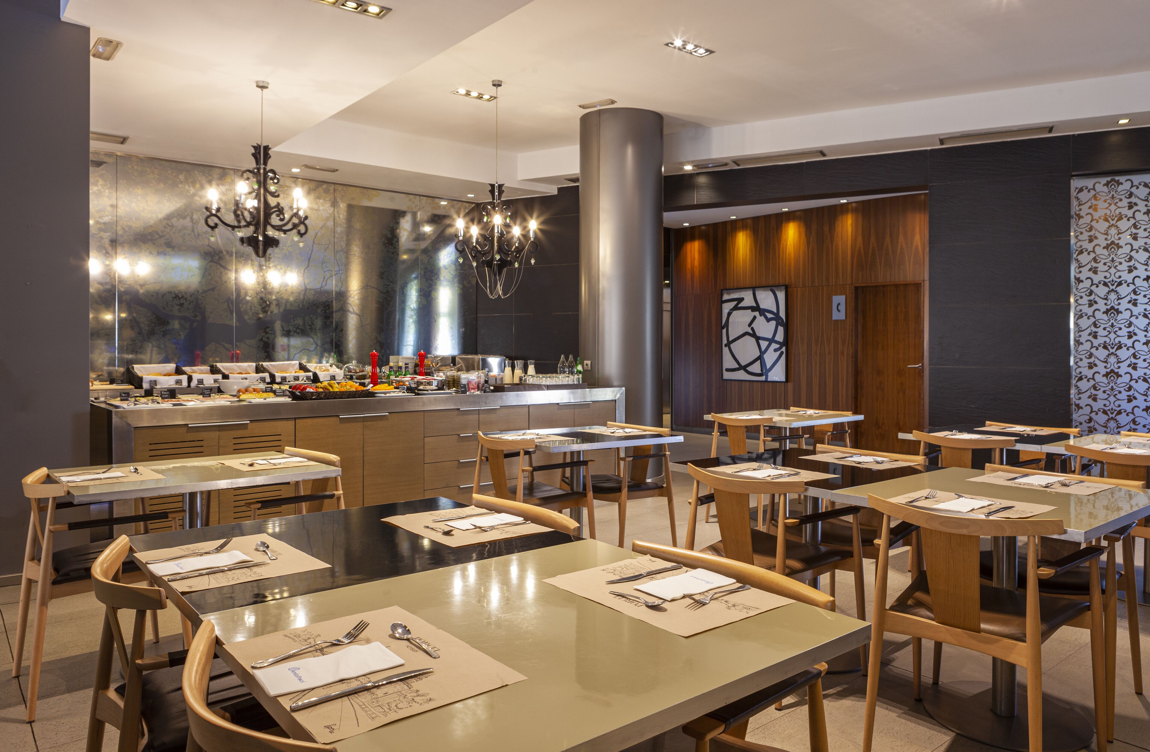 Un restaurante moderno con varias mesas, una zona de bar central y una gran lámpara de araña.