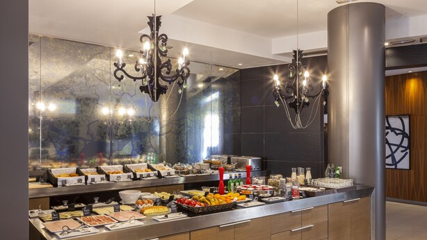 A buffet with various food items and beverages, modern decor, and a large mirror reflecting the room. - Hotel Porcel Torneo (Seville)