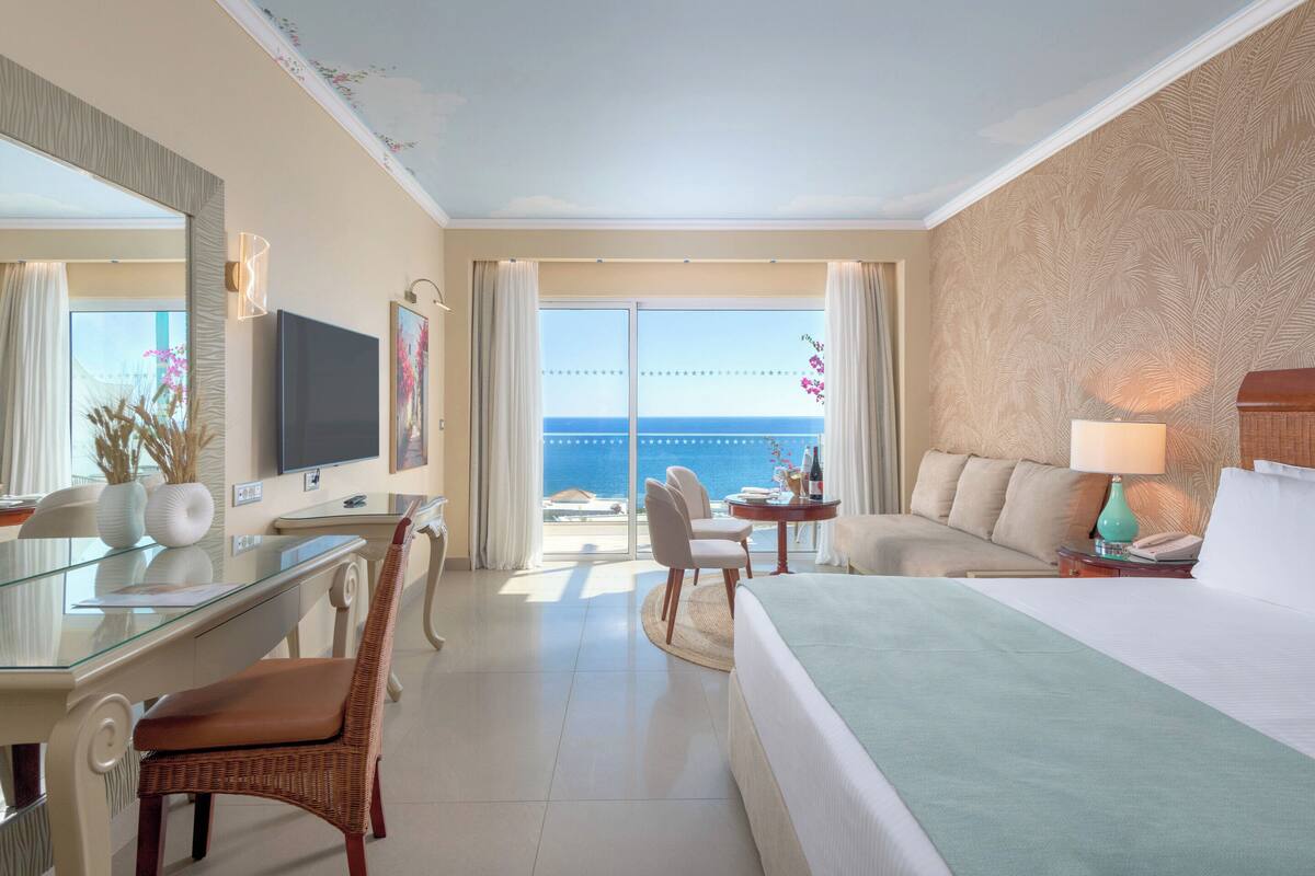 Een hotelkamer met een groot bed, een bureau met stoel, een televisie en uitzicht op de oceaan.