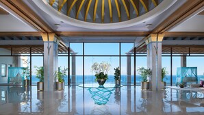 Un hall amplio con suelo de cristal, ventanas grandes y una mesa central con un jarrón de flores.