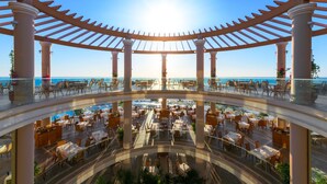 Un área de comedor al aire libre con varios niveles y vistas despejadas al océano, rodeada de columnas y una estructura de pérgola.