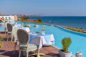 A dining area with tables and chairs by a pool, overlooking the sea. - Atrium Prestige Thalasso Spa Resort & Villas (Rhodes)
