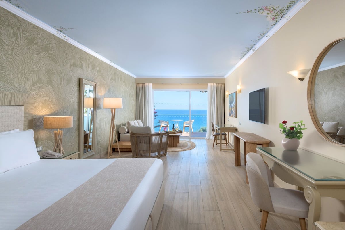 Een hotelkamer met een groot bed, een bureau, een stoel, een tafel en uitzicht op de oceaan.