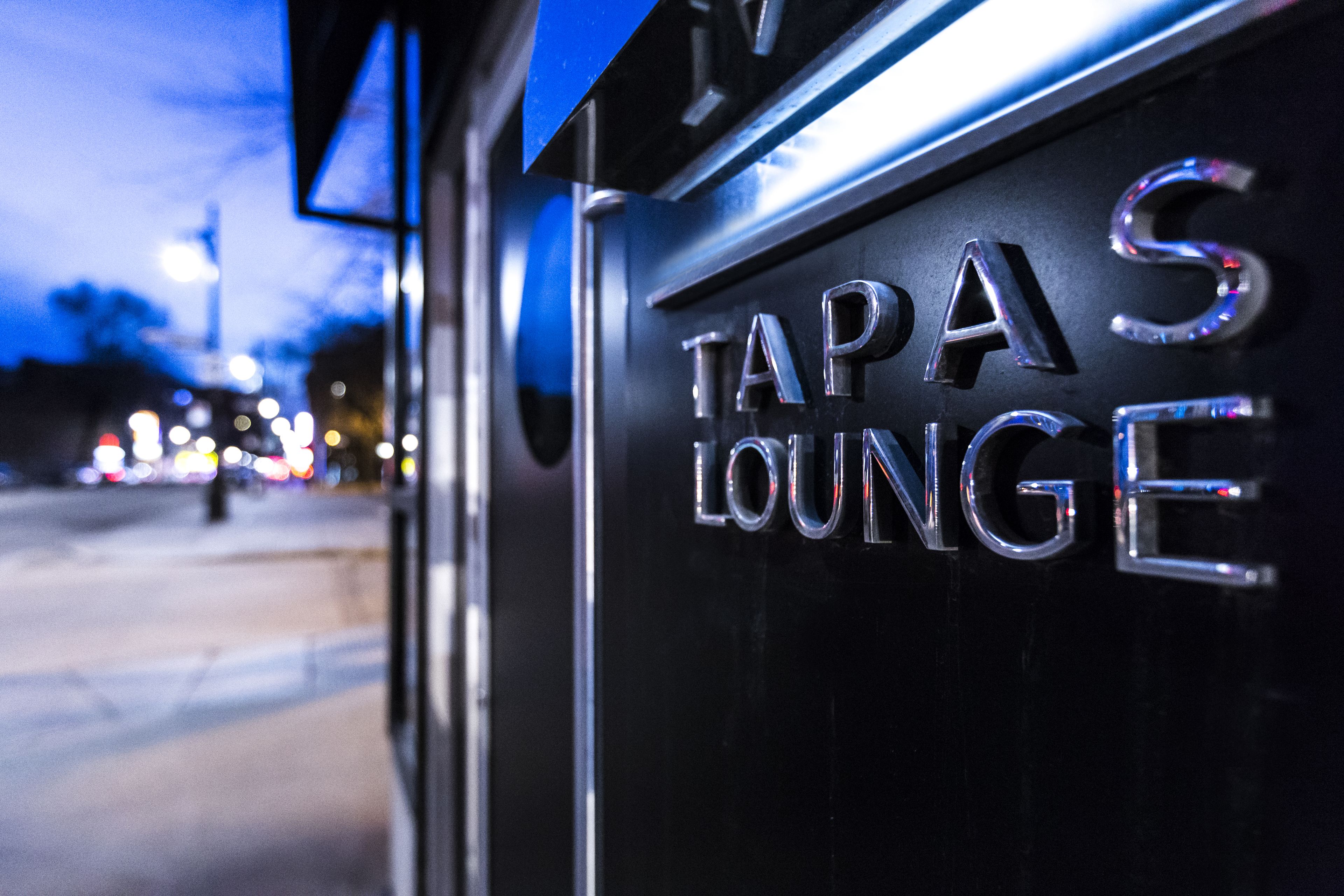 A sign for "TAPA'S LOUNGE" with a metallic finish and reflective letters.