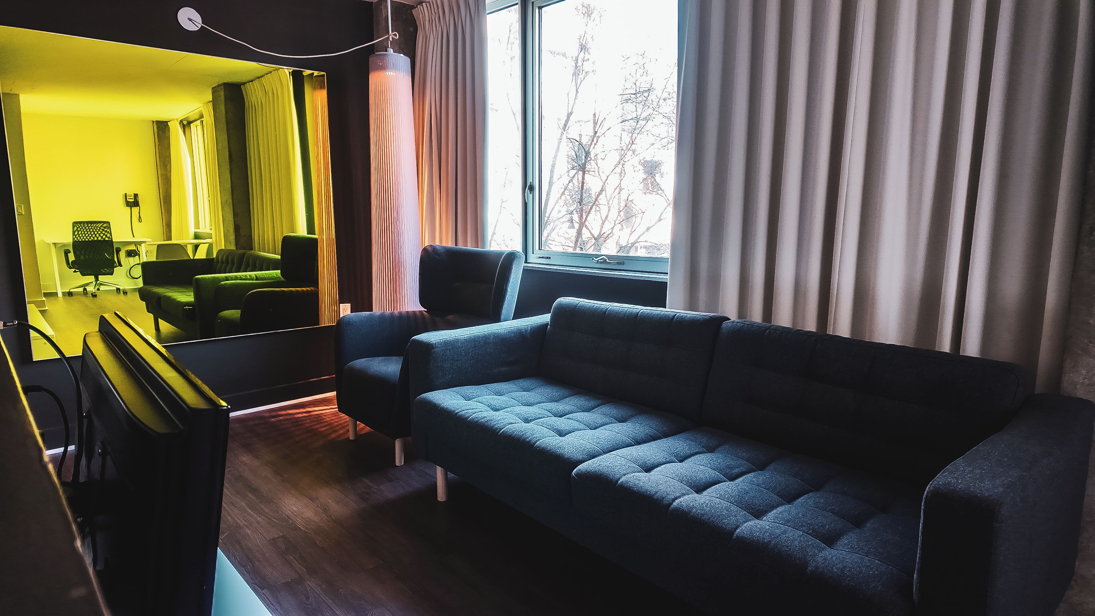 A modern living room with a sofa, a chair, a desk, and a mirror reflecting the room.