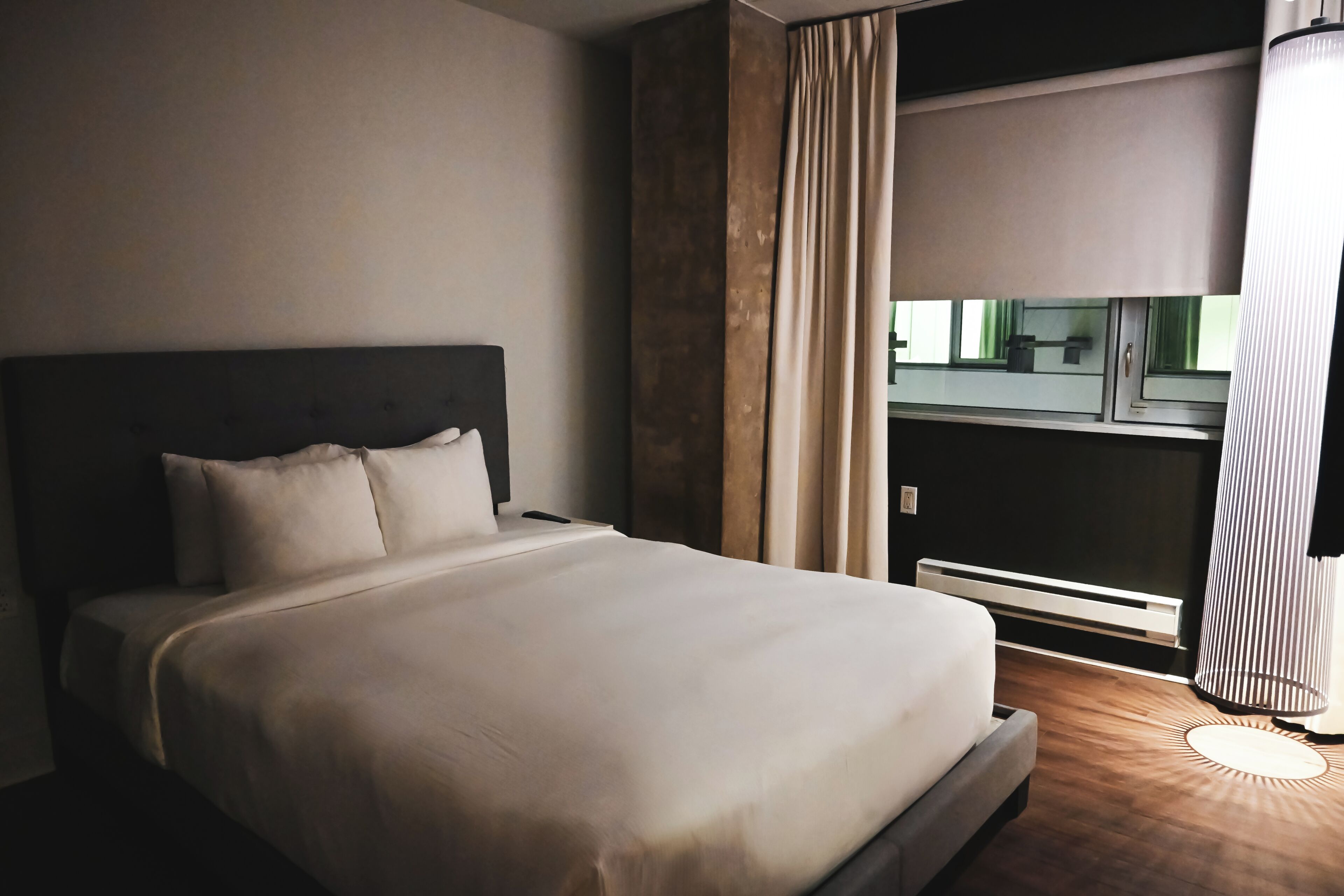 A hotel room with a large bed, a nightstand, a lamp, a window with curtains, and a view of the outside.