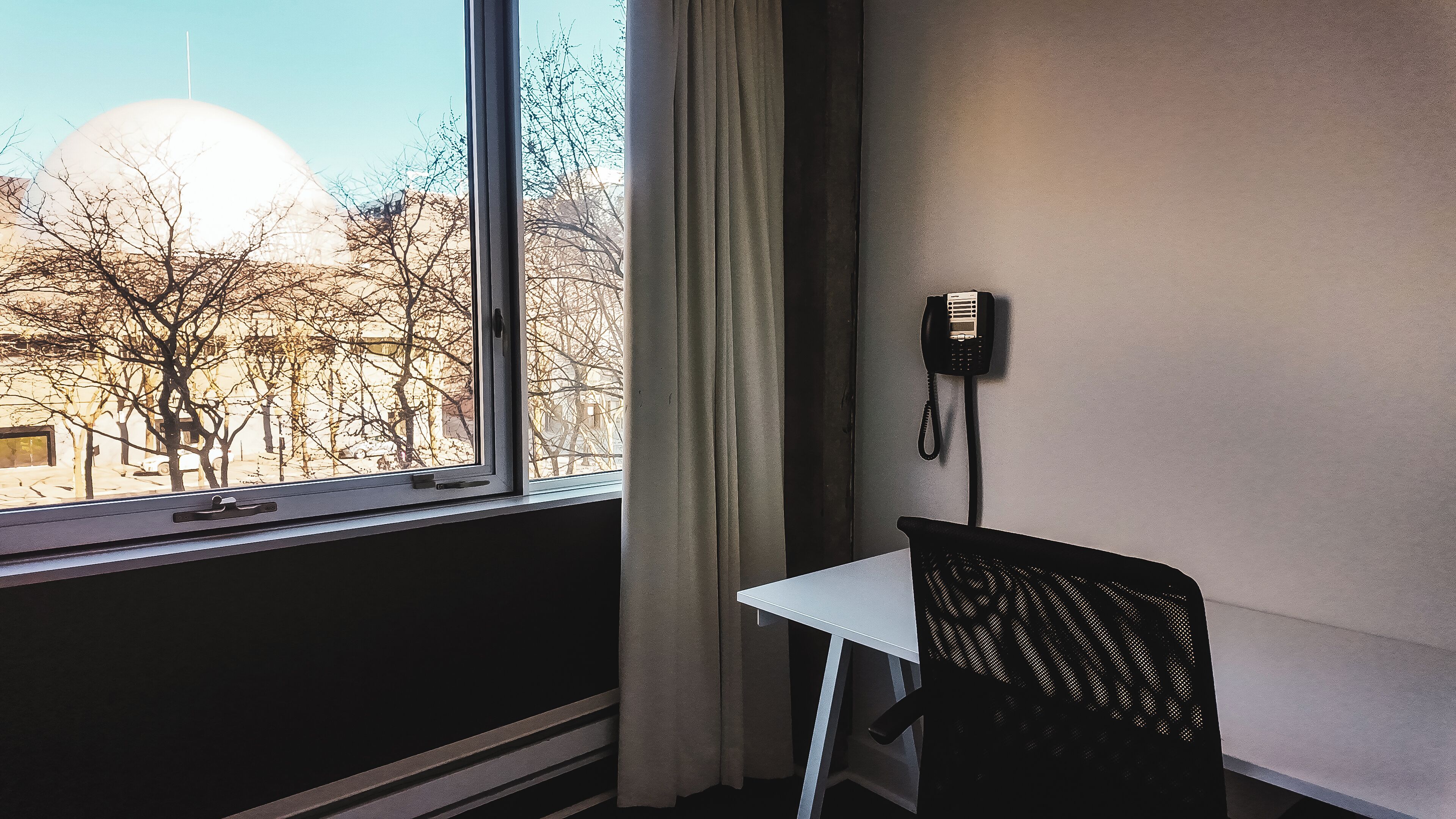 Een kamer met raam, stoel, tafel en telefoon.