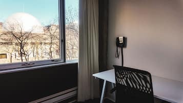 Een kamer met raam, stoel, tafel en telefoon.