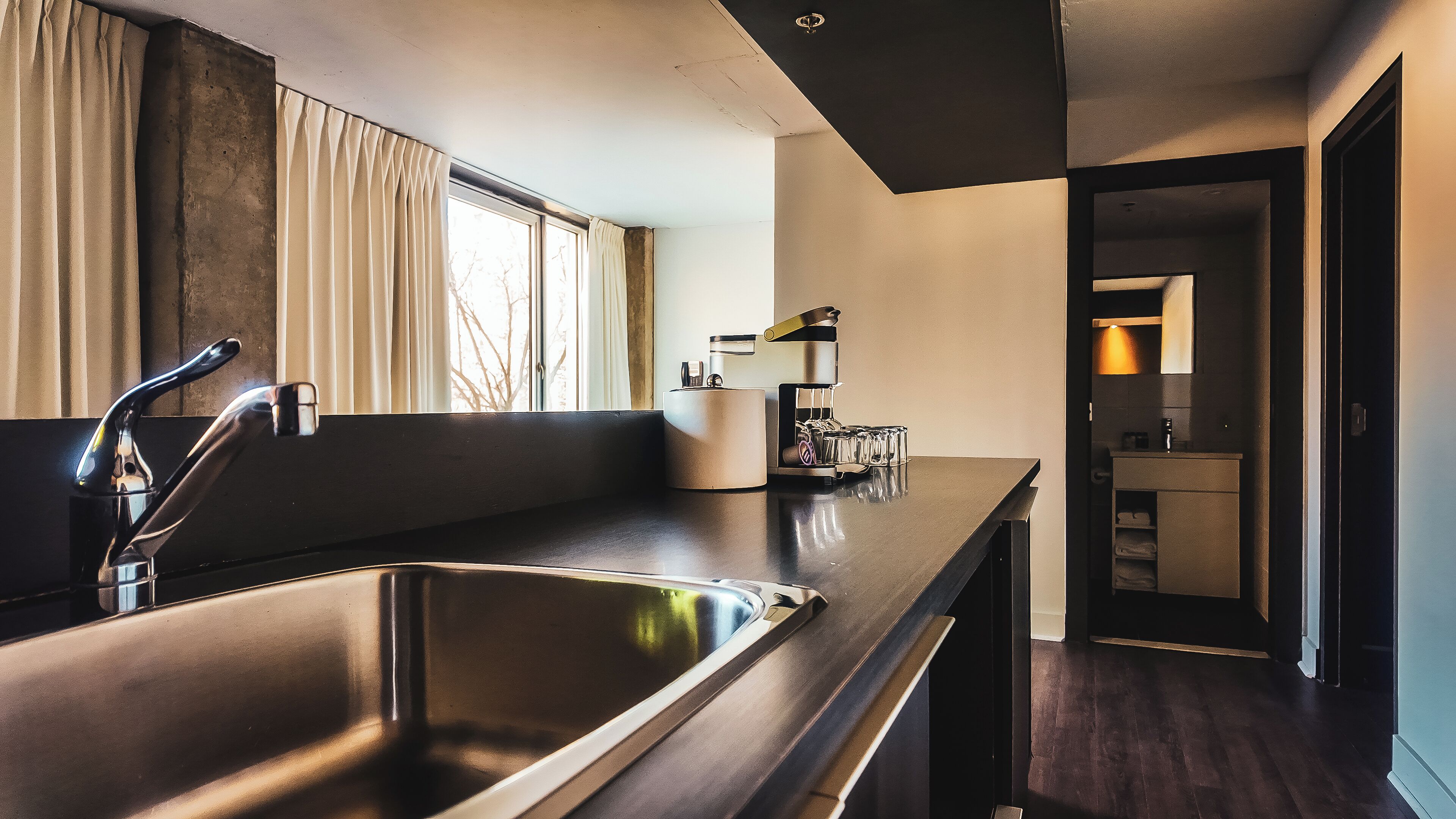 A modern kitchen with a stainless steel sink, a coffee machine, and a window with curtains.
