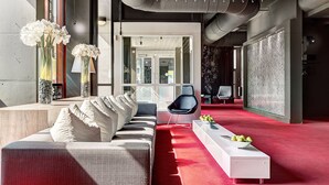 Un hall d’hôtel moderne avec un tapis rouge, un canapé avec des coussins blancs, un fauteuil noir et une console blanche ornée de pommes.