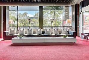 A modern seating area with a sofa and cushions, a coffee table, and a view of trees and mountains through large windows.
