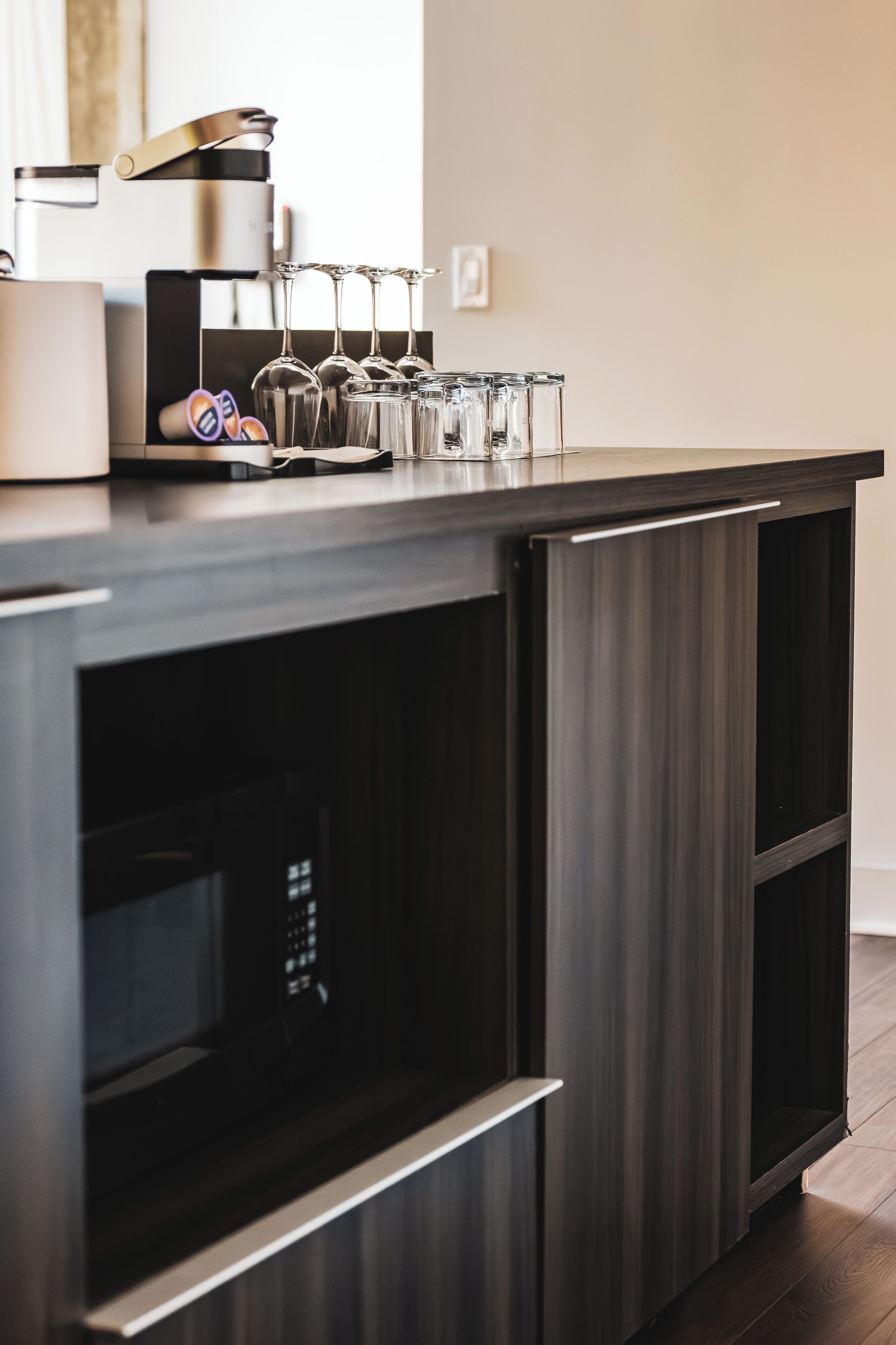 Una cocina moderna con cafetera espresso integrada, copas de vino y microondas.