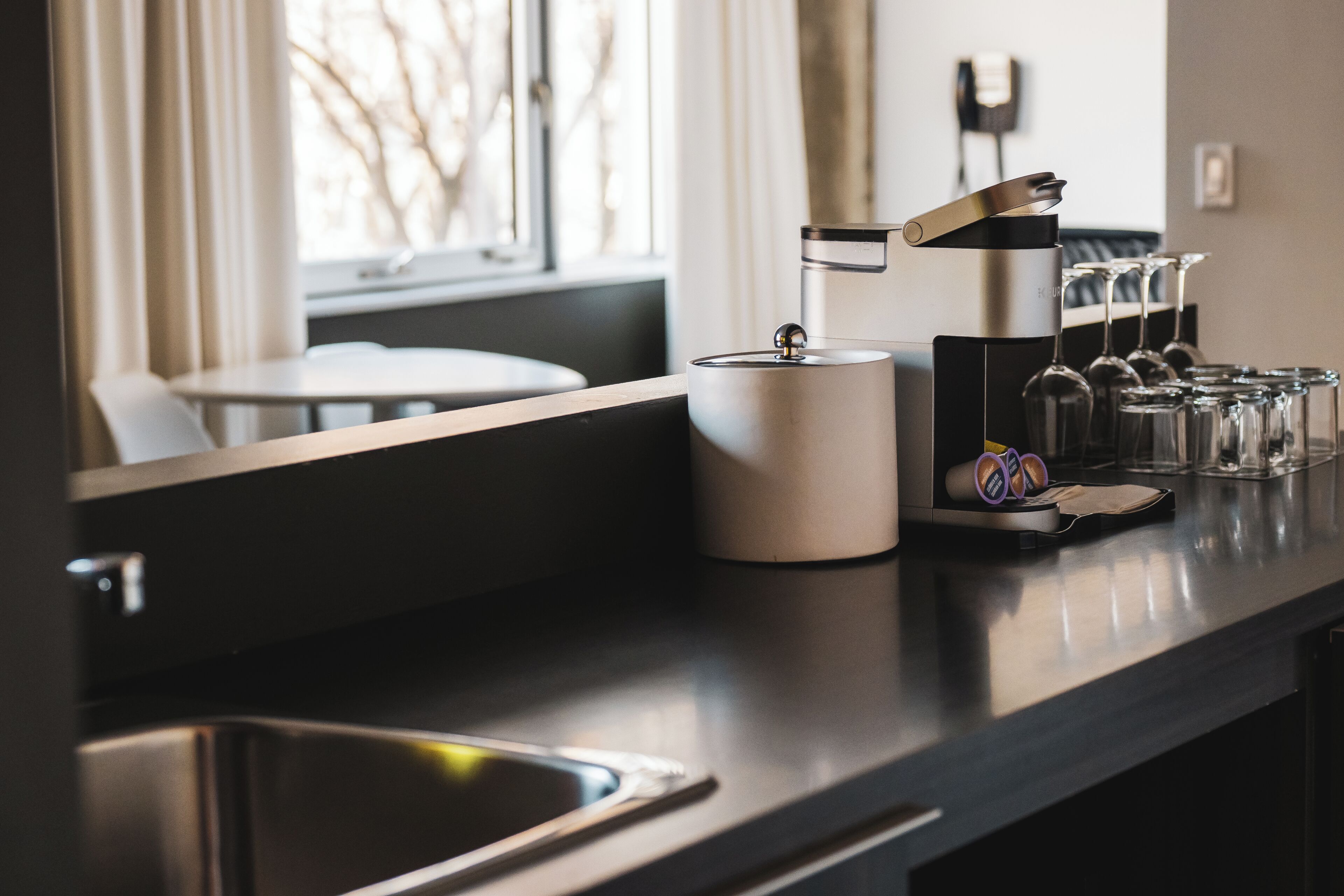 Eine moderne Küche mit einer Spüle aus Edelstahl, einer Kaffeemaschine und einem Weinkühlschrank aus Glas.