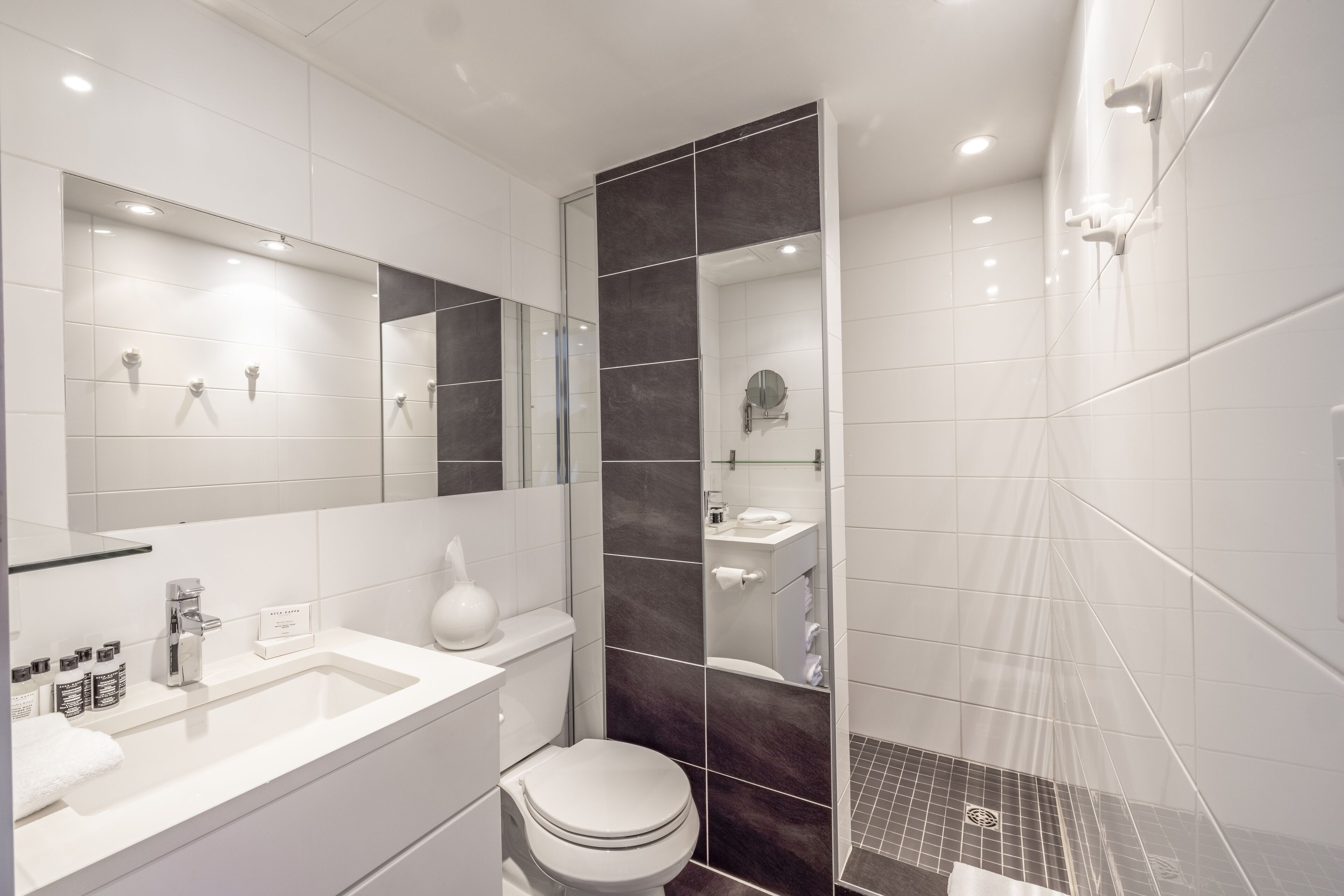 Un baño moderno con un espejo grande, lavamanos blanco y zona de ducha.