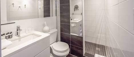 Un baño moderno con un espejo grande, lavamanos blanco y zona de ducha.