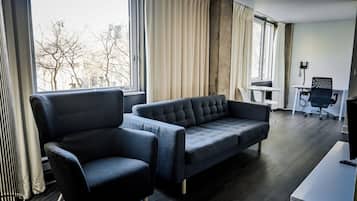 A modern hotel room with a sofa, armchair, and a desk with a chair.