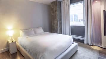Una habitación de hotel moderna con una cama grande, una mesita de noche con lámpara, un ventanal con cortinas y una lámpara de pie.